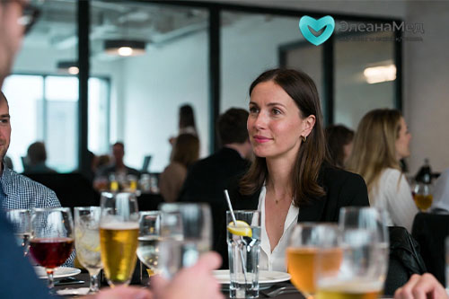 Женщина 35 лет с бокалом минеральной воды с лимоном на корпоративе среди коллег с алкоголем